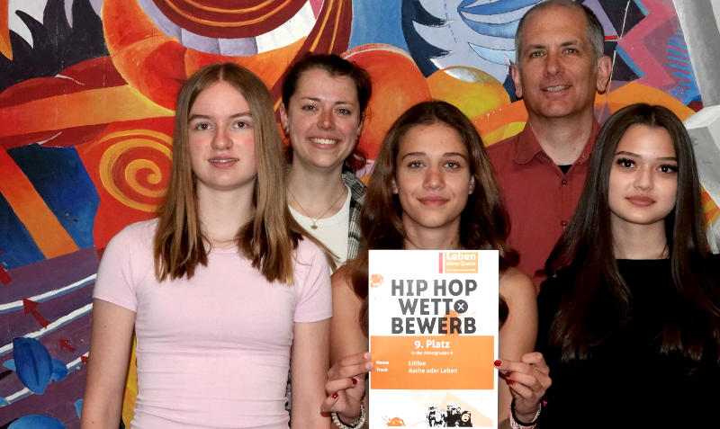 Schulleiter Dr. Heidbüchel mit Schülerinnen und einer Urkunde über den 9. Platz beim HipHop Wettbewerb "Leben ohne Qualm"